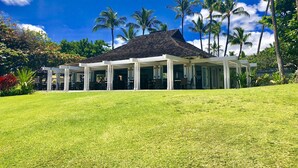 A covered outdoor area with a tiled roof, surrounded by a well-maintained lawn and palm trees. - Best of Mauna Lani! Clean, Spacious Resort Townhome, Pool/Beach Club!  (KAMUELA)