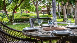 A round table set for dining outdoors with chairs, surrounded by lush greenery and trees. - Best of Mauna Lani! Clean, Spacious Resort Townhome, Pool/Beach Club!  (KAMUELA)