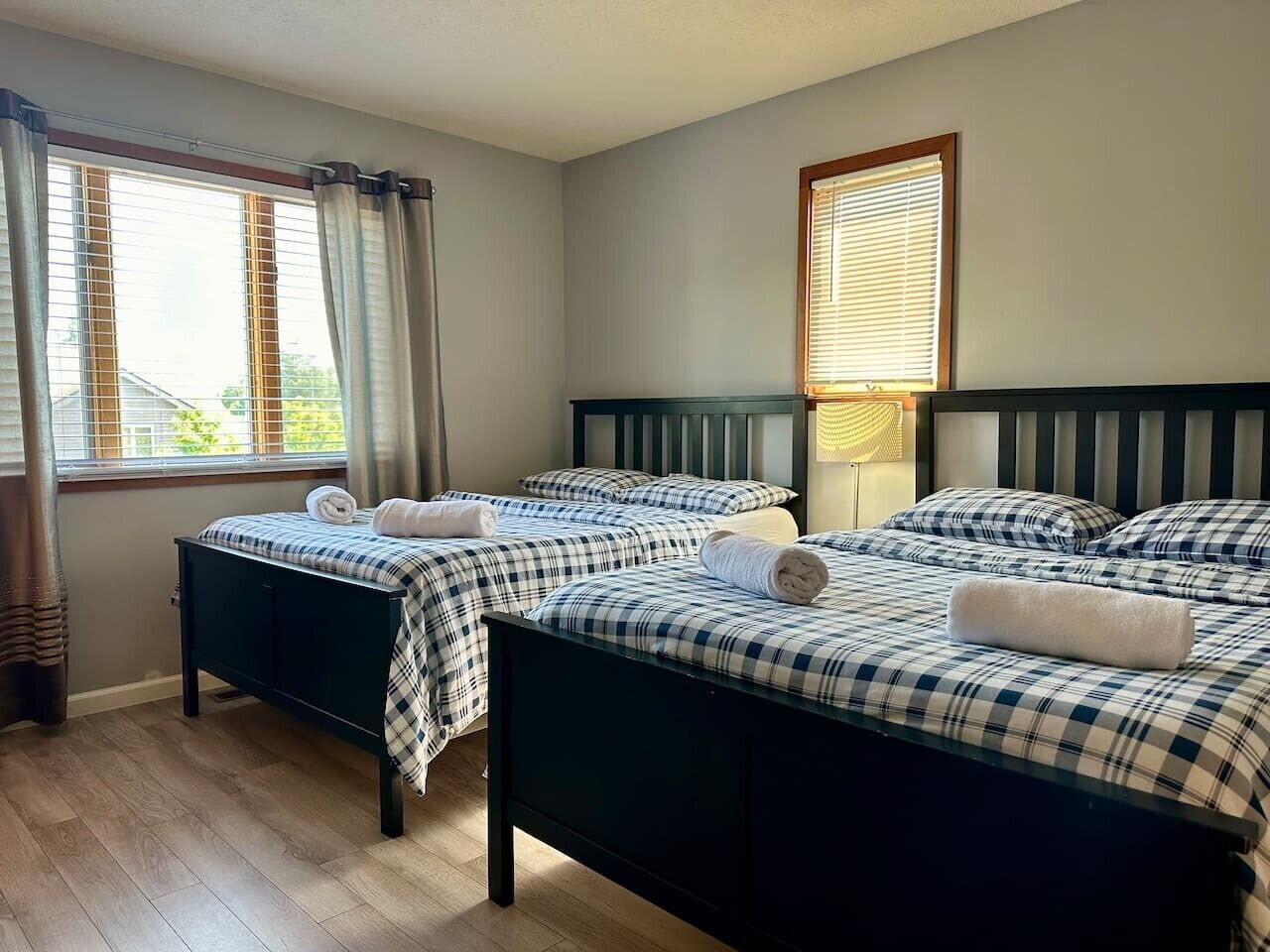 Una habitación con dos camas, cada una con colcha a cuadros y toallas blancas, una ventana con persianas y una lámpara en la mesita de noche.