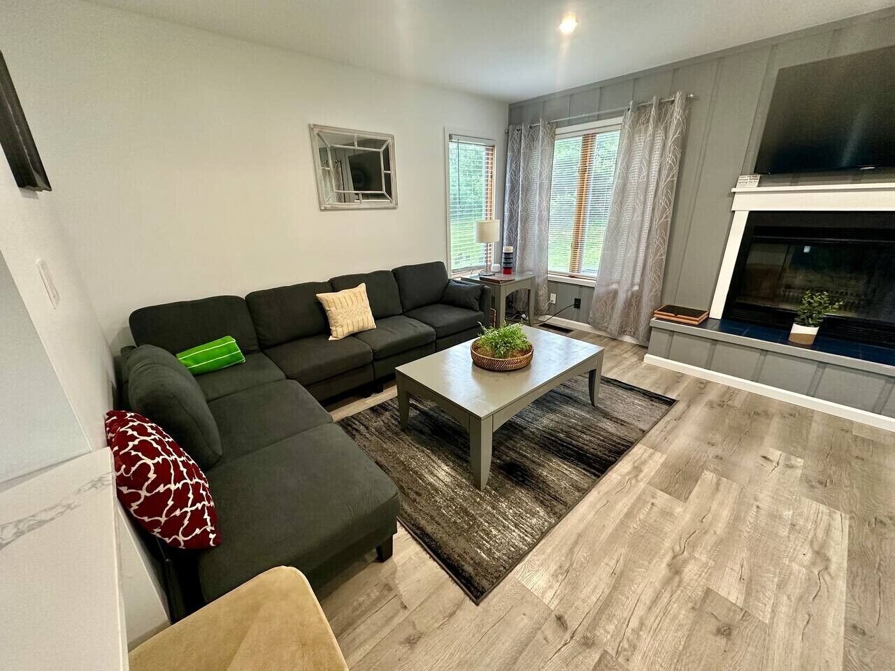 A living room with a sectional sofa, a coffee table, a fireplace, and a large window with curtains.