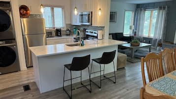 Une cuisine moderne dotée d’un îlot central, de tabourets de bar et d’un coin repas avec des chaises en bois.