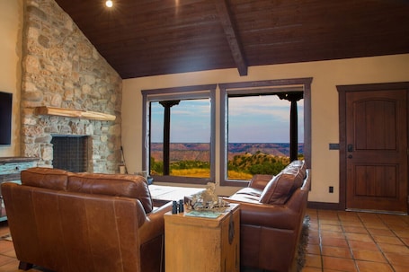 A living room with a stone fireplace, leather sofas, and a view of a canyon.