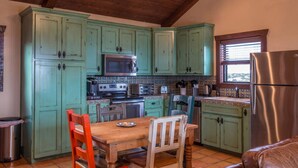 Une cuisine avec des meubles de couleur verte, une table en bois et un réfrigérateur en acier inoxydable.