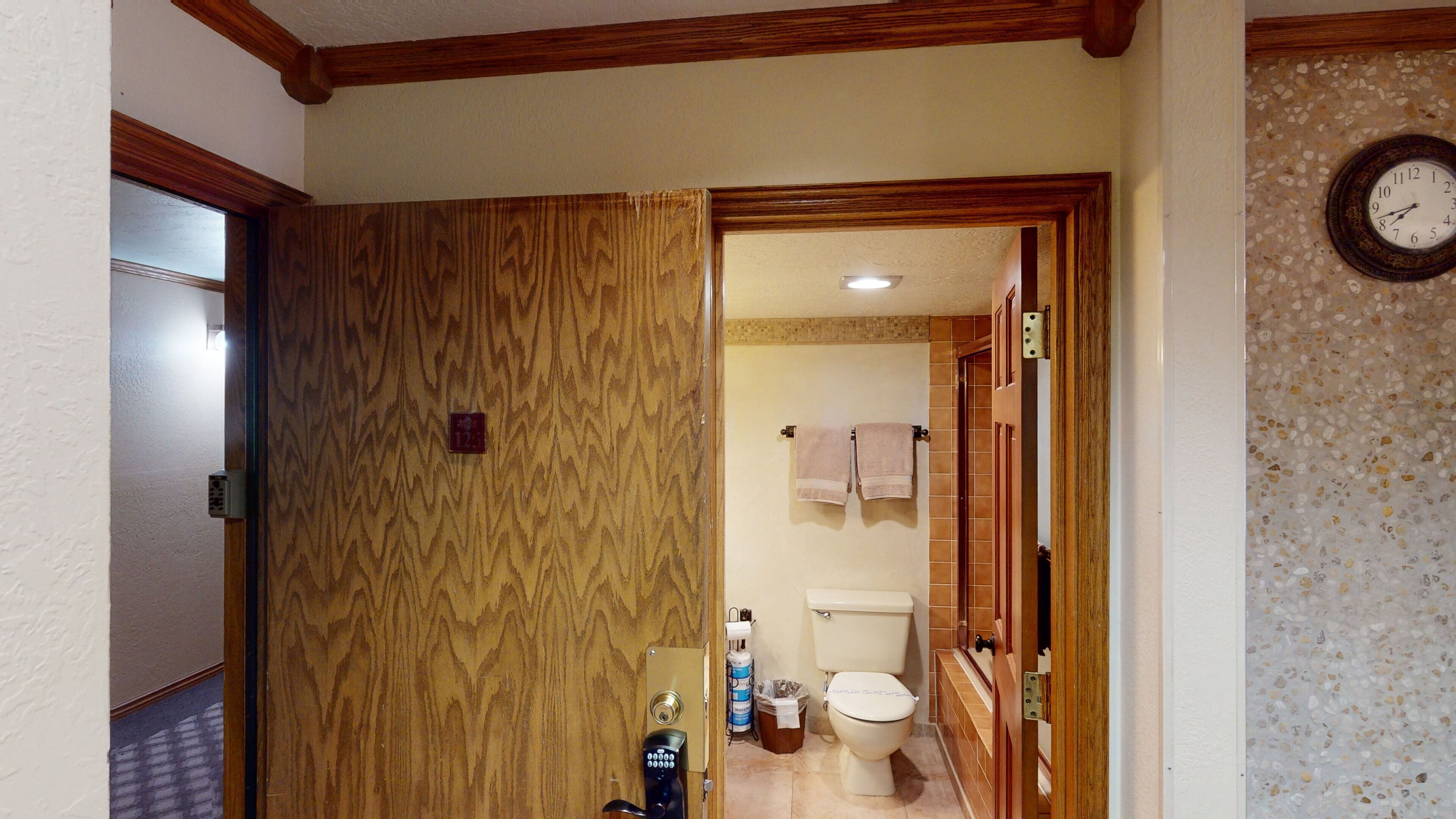 A bathroom with a toilet, a towel rack, and a clock on the wall.