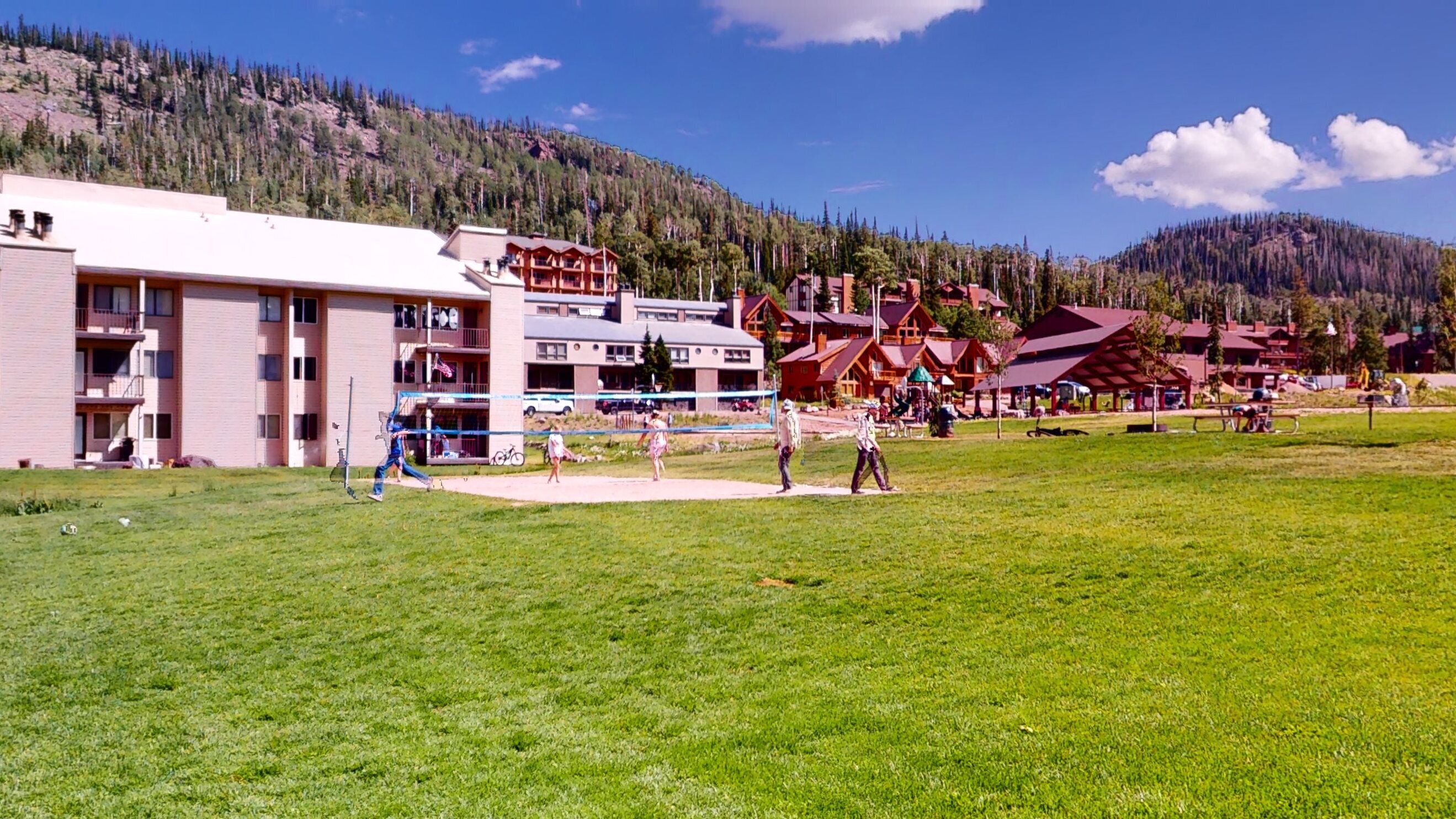 A hotel with multiple buildings, a grassy field, and a mountainous backdrop.