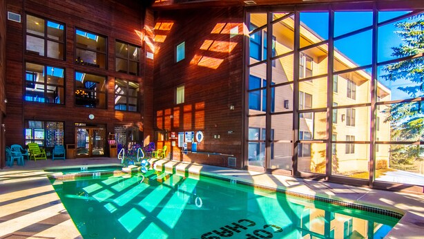 A swimming pool with a sunlit interior, surrounded by large windows and a wooden building facade. - Brian Head Platinum Studio, Pool-Jacuzzi, Ski-In/Out, , Sleeps 7,  Elevator (Brian Head)