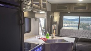 Eine kompakte Küchenzeile für Wohnmobile mit integriertem Kochfeld, Spüle und Fenster mit schöner Aussicht.