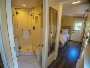 A hotel bathroom with a glass shower enclosure, a toilet, and a bed with a sign indicating a laundry room.