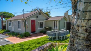 A single-story house with a red door, a small porch, and a lawn. - Green Beach House 500' to the Waves- Electric Vehicle Charger! (Laguna Beach)