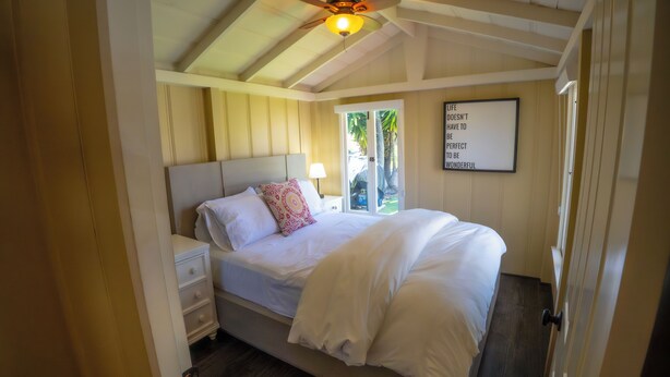 A bedroom with a bed, a nightstand, a wall-mounted light, and a motivational quote on the wall. - Green Beach House 500' to the Waves- Electric Vehicle Charger! (Laguna Beach)