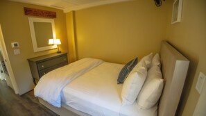 A hotel room with a bed, a nightstand, a lamp, a mirror, and a sign on the wall.