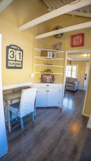 A room with a desk, wicker chair, white cabinets, a clock, and a sofa.