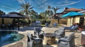 Une terrasse extérieure avec une piscine, des chaises longues, un foyer et un barbecue.