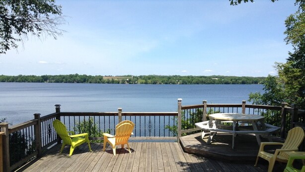 A wooden deck with a view of a lake, featuring a table and chairs.