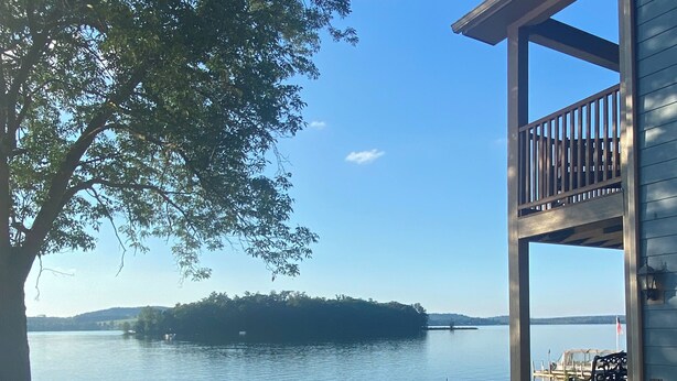 A patio with outdoor furniture overlooking a lake, a wooden deck, and a view of distant hills. - Luxurious Lakefront Living With Amenities close to Cooperstown (Richfield Springs)