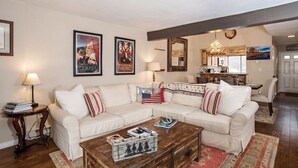 A living room with a sectional sofa, a coffee table, and a kitchen in the background.
