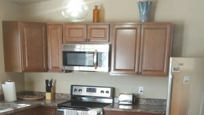 A kitchen with wooden cabinets, a microwave, a stove, a refrigerator, and a trash bin. - Remodeled 2 Bedroom, 2 Bath apartment with Hot Tub.   (belgrade)
