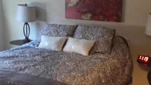 A bedroom with a bed, a ceiling fan, a nightstand, a lamp, a clock, and a floral painting on the wall. - Remodeled 2 Bedroom, 2 Bath apartment with Hot Tub.   (belgrade)