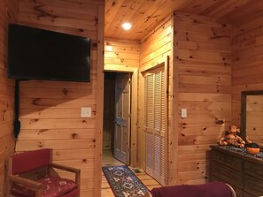 A wooden cabin interior with a television mounted on the wall, a chair, a small table with a pumpkin decoration, and a door leading to another room. - Beautiful cabin close to downtown Boone (Boone)