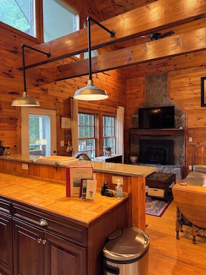 A wooden cabin interior with a kitchen area, stone fireplace, and a large window. - Beautiful cabin close to downtown Boone (Boone)