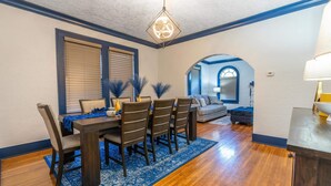 Un coin repas avec une table en bois, des chaises et un tapis bleu. Un lustre est suspendu au-dessus de la table et une lampe se trouve sur une table d’appoint.
