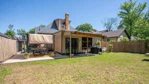 Un jardin avec un patio couvert, un espace barbecue et une cour clôturée.