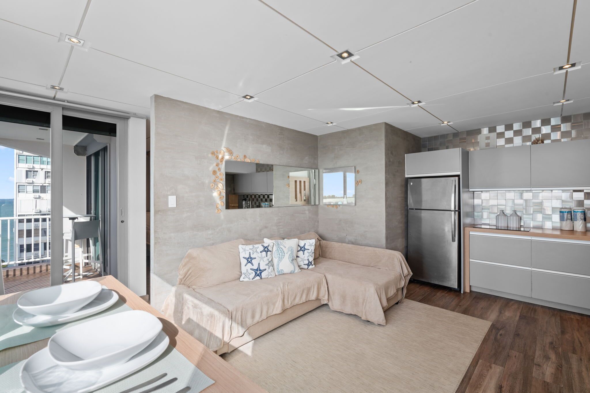 Een moderne keuken met een ingebouwde koelkast, een zithoek met een beige bank en uitzicht op het balkon.