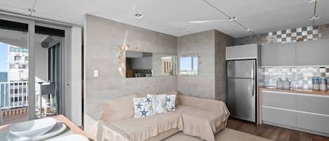 Una cocina moderna con refrigerador empotrado, una zona de comedor con sofá color beige y vistas al balcón.