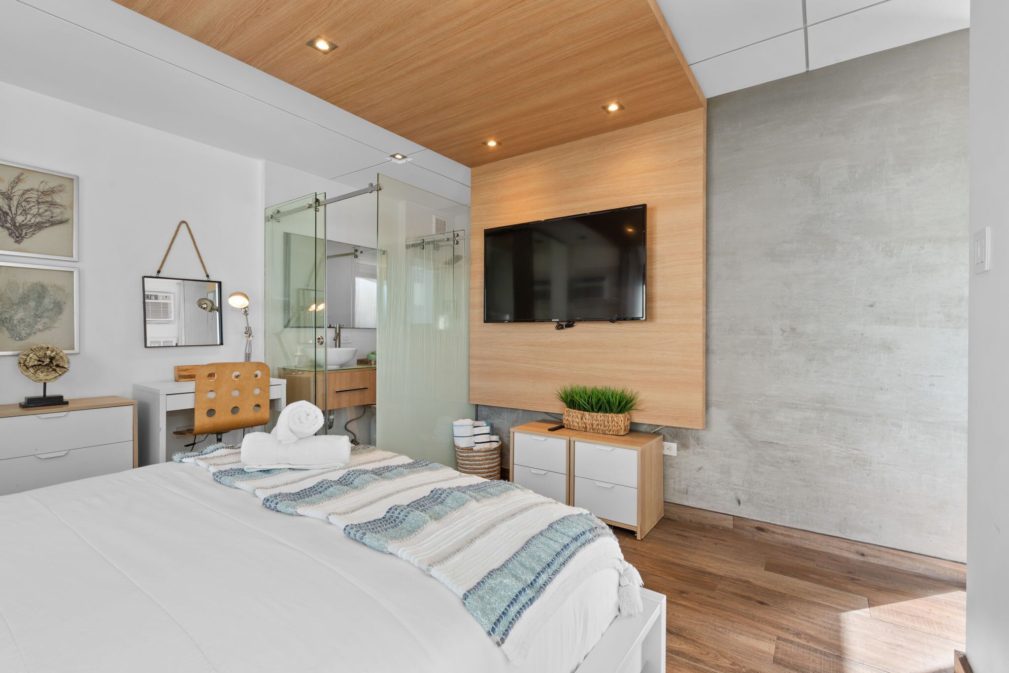 A modern bedroom with a large bed, a TV mounted on the wall, and a wooden ceiling.