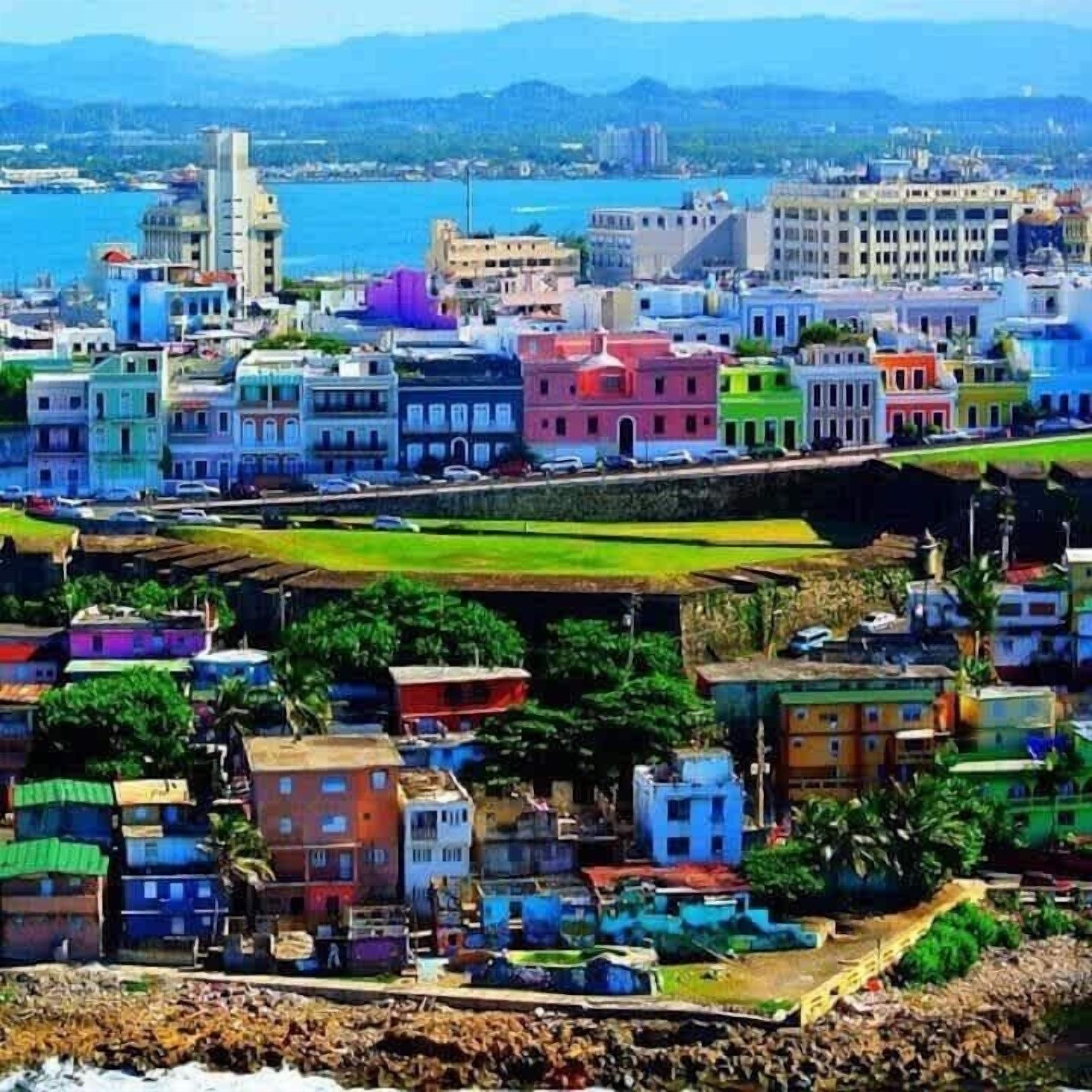Un paisaje costero con edificios coloridos, un puerto deportivo y una cadena montañosa distante.