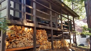 Une cabane en bois à plusieurs niveaux, avec une grande pile de bois de chauffage bien visible au premier plan.
