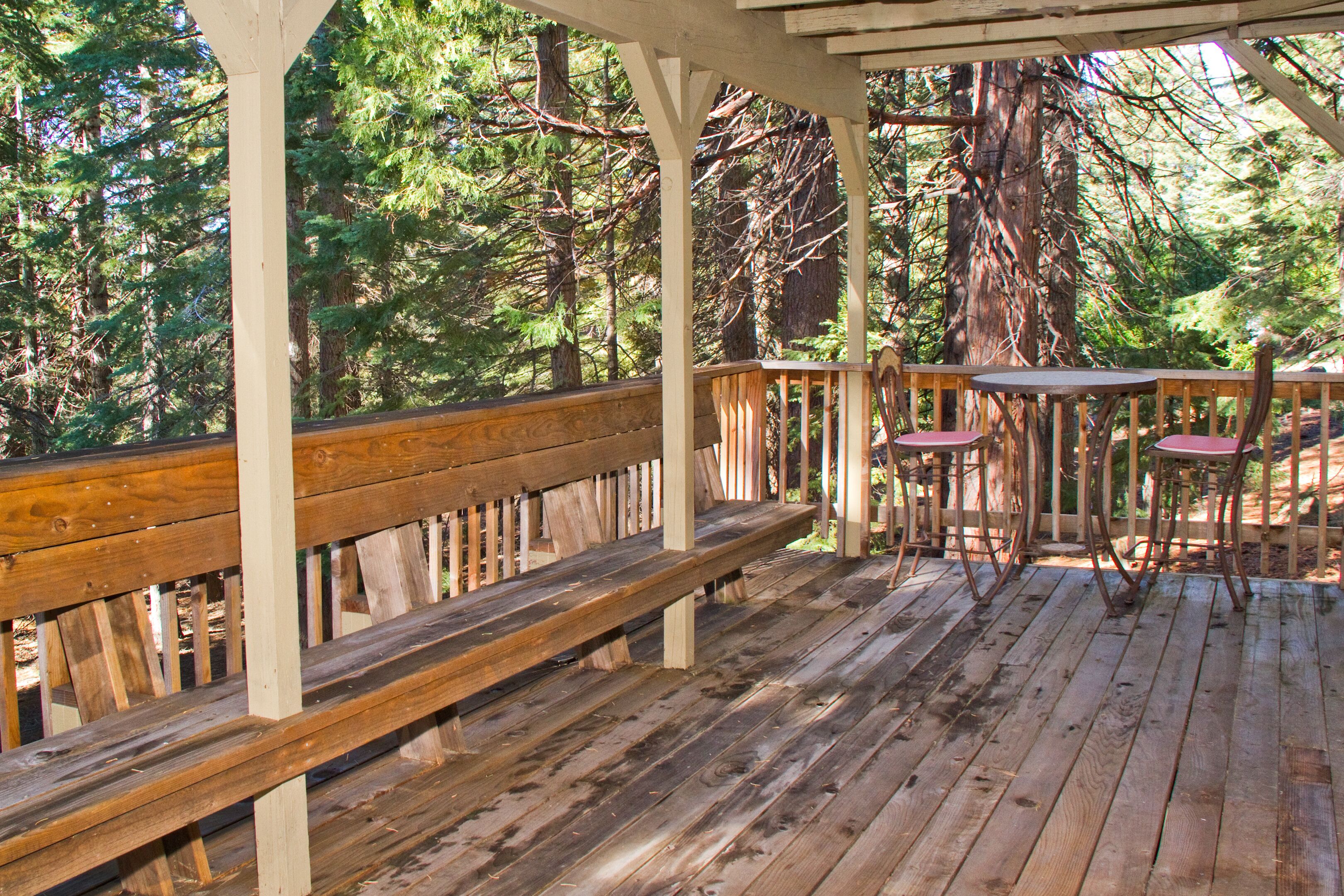 Una terraza de madera con bancos y mesas, rodeada de un bosque.