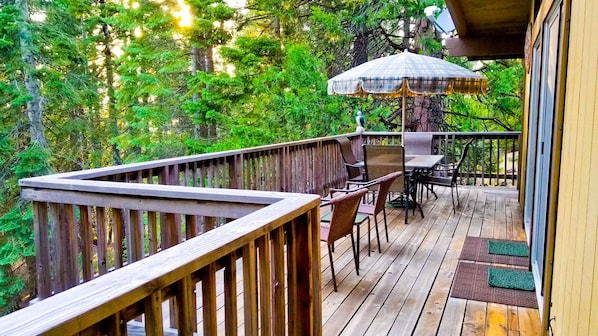 A wooden deck with a table and chairs, surrounded by lush greenery.