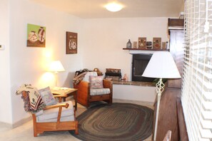 A cozy living room with a fireplace, a wooden chair, a small table, and a lamp.