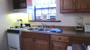A kitchen with wooden cabinets, a gas stove, a sink, and a window with curtains. - Perfect for Travel Nurses, Professionals or Relocation to Santa Fe! (Santa Fe)