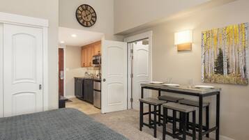 A bedroom with a bed, a dining area with a table and chairs, a kitchen with cabinets and appliances, and a wall clock.