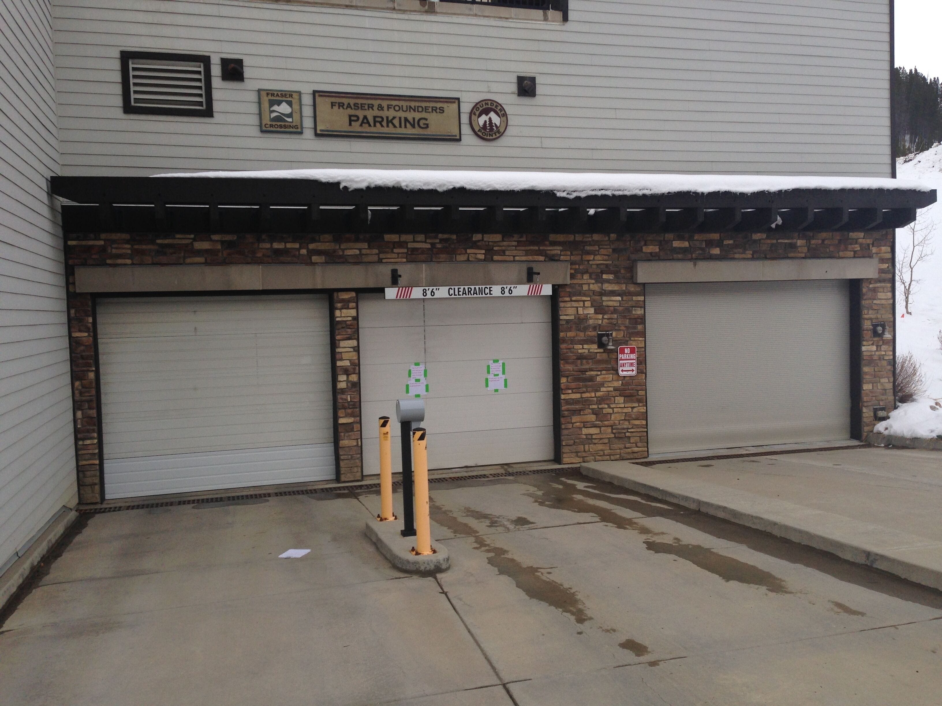 A building with two garage doors, a sign indicating parking, and a no parking sign.