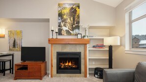 A living room with a fireplace, a television, a sofa, and artwork on the walls. - Top Floor Ski-In / Ski-Out Studio Condo at the base of Winter Park Resort (Winter Park)