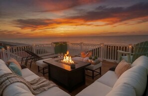 A deck with a fire feature, outdoor seating, and a view of the ocean at sunset. - 🌞Oceanfront Rooftop getaway 🏖️Steps to sand 🐶Dog Friendly⚡️EV charger (North Topsail Beach)