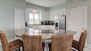 A kitchen with a central island, white cabinets, and woven chairs. - 🌞Oceanfront Rooftop getaway 🏖️Steps to sand 🐶Dog Friendly⚡️EV charger (North Topsail Beach)