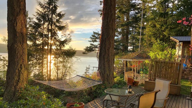 A deck with a table and chairs, overlooking a lake with trees and a gazebo in the background.