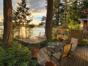 A deck with a table and chairs, overlooking a lake with trees and a gazebo in the background.