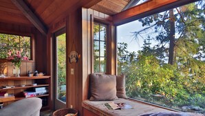 A cozy cabin interior with a wooden bench, a basket, and a window offering a view of trees and foliage.