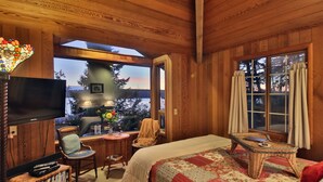 A cozy cabin room with a bed, a television, a small table, and a chair.