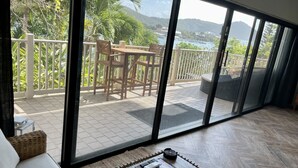 Una habitación con un amplio ventanal corredero que da a un balcón exterior con vistas a una masa de agua y colinas.
