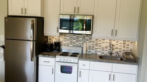 Cocina compacta con armarios blancos, un refrigerador de acero inoxidable, microondas, estufa y pileta.