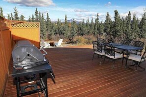 A wooden deck with a grill, outdoor table, and chairs.