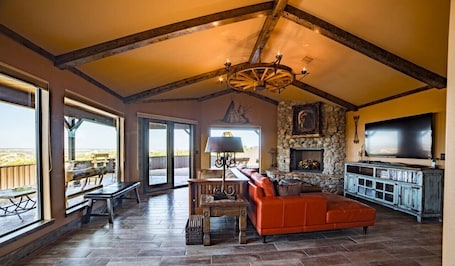 A spacious living room with a stone fireplace, a large TV, and a red leather sofa.
