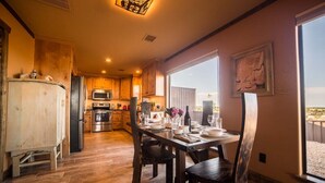 A modern kitchen with wooden cabinets, a stainless steel refrigerator, and a dining area with a table set for four. - Comanche cabin on the west rim (Canyon)