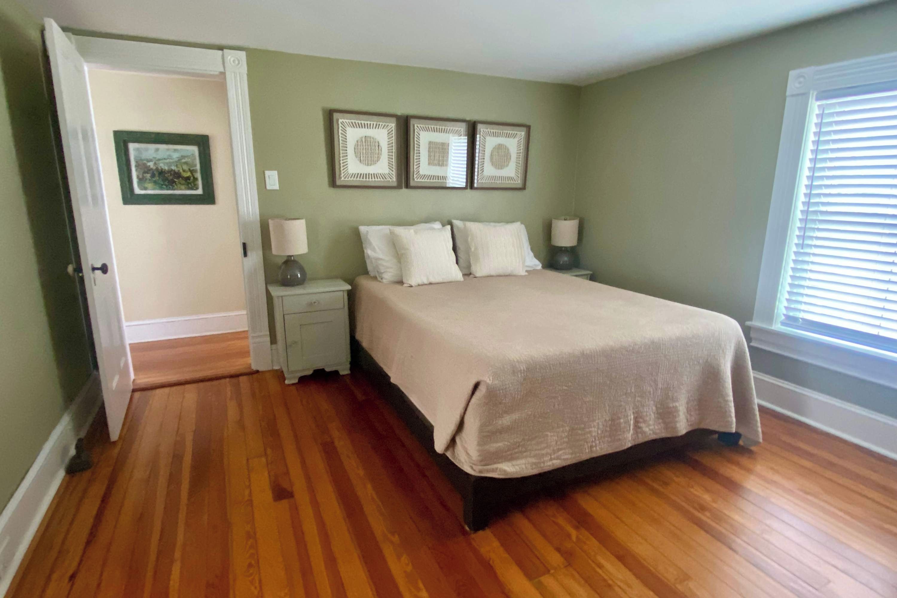 A bedroom with a bed, two bedside tables, a door, and a window with blinds.